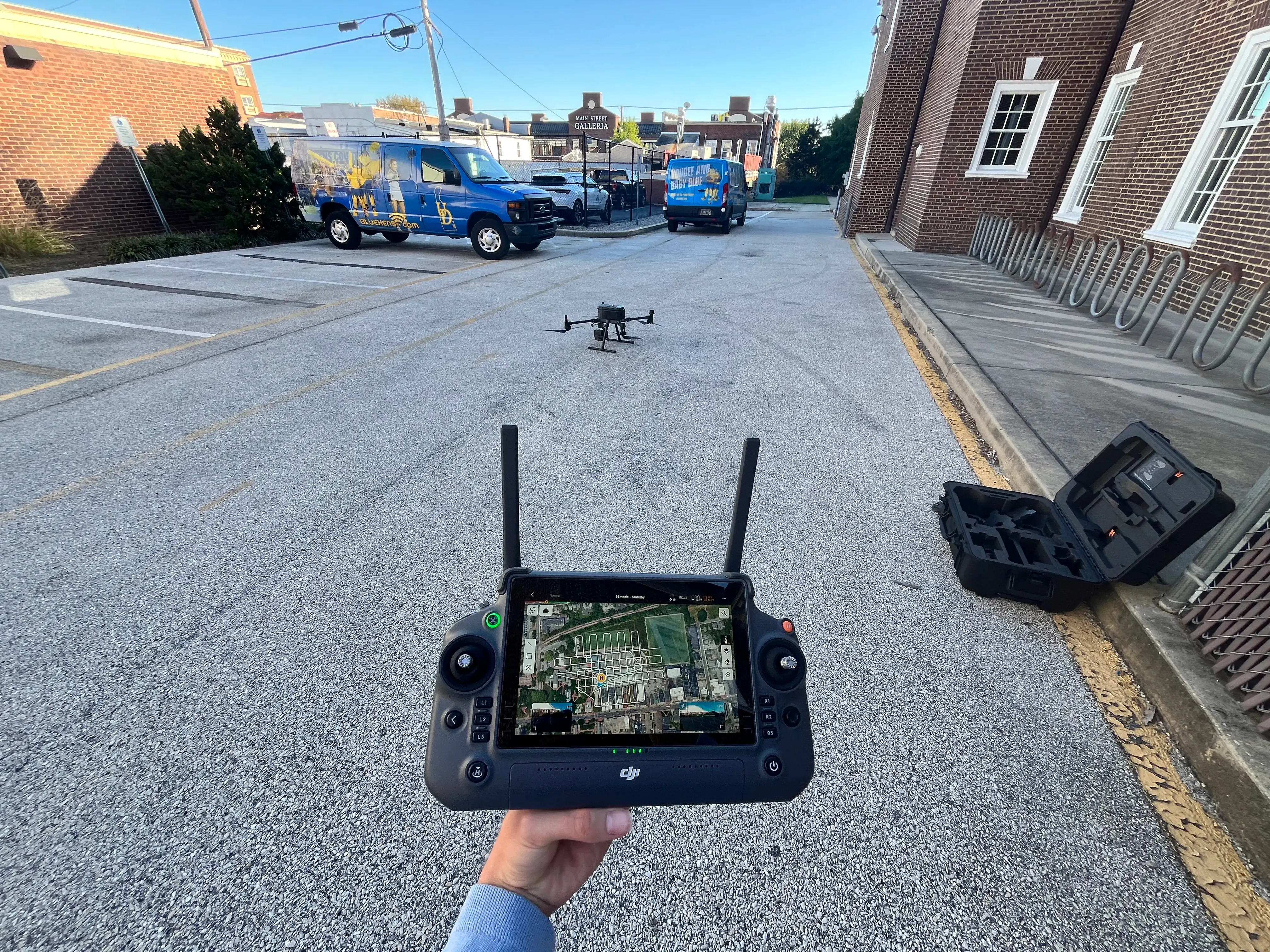 DJI Matrice 350 RTK drone hovering above a parking lot during an autonomous flight test, controller in the foreground